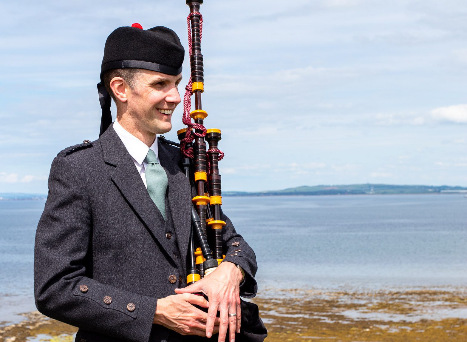 Ayrshire Bagpiper Alistair Brown standing with his bagpipes and wearing lamont kilt at Greenan Shore in Ayr, Scotland